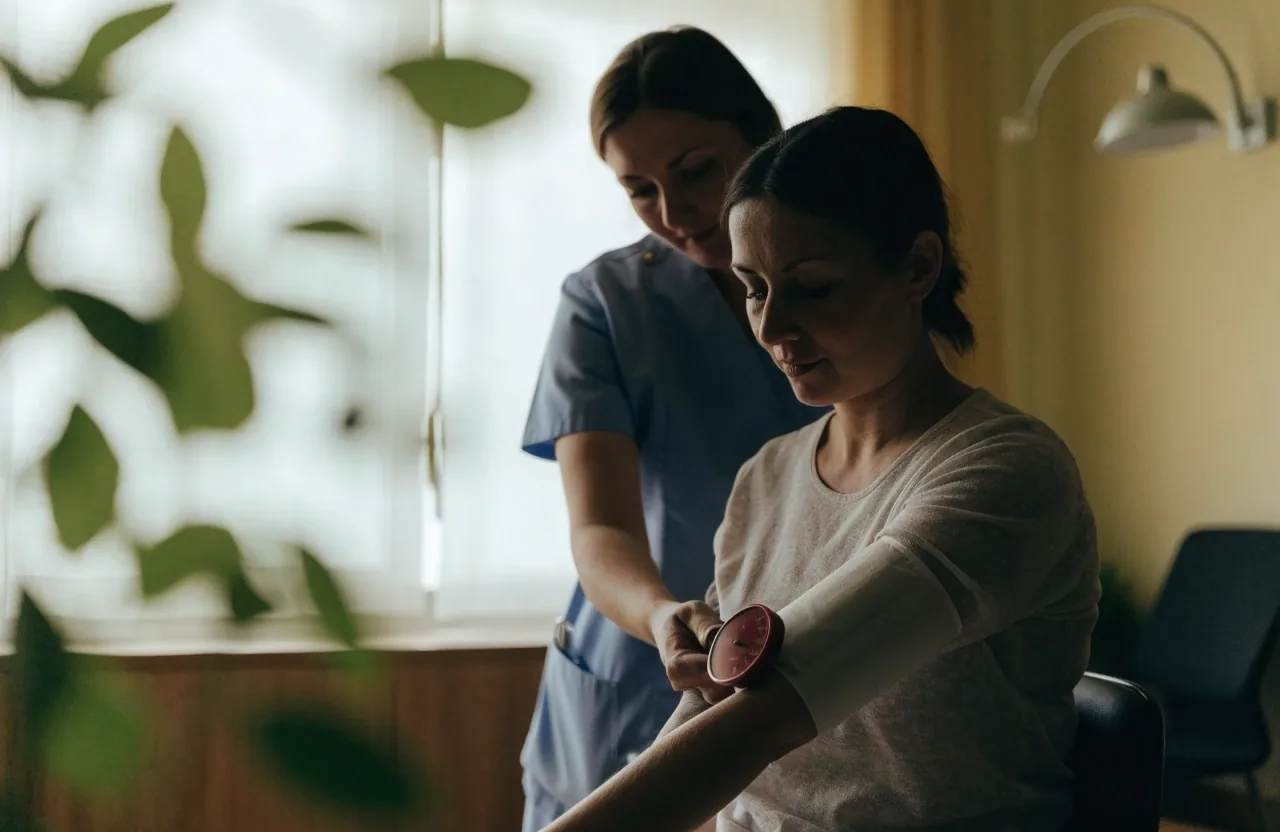 A blood pressure cuff being adjusted on a patient's forearm in a clinic room